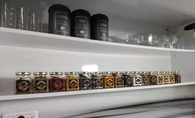 צנצנות זכוכית עם תבלינים מסודרות לצד מכלי מתכת על מדפי מטבח